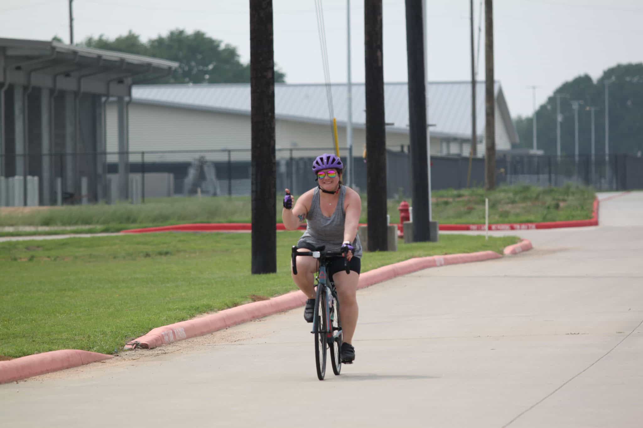 Bright woman riding bicycle with purple helmet on a scenic bike trail in Texas, promoting Bluebonnet Express cycling event.