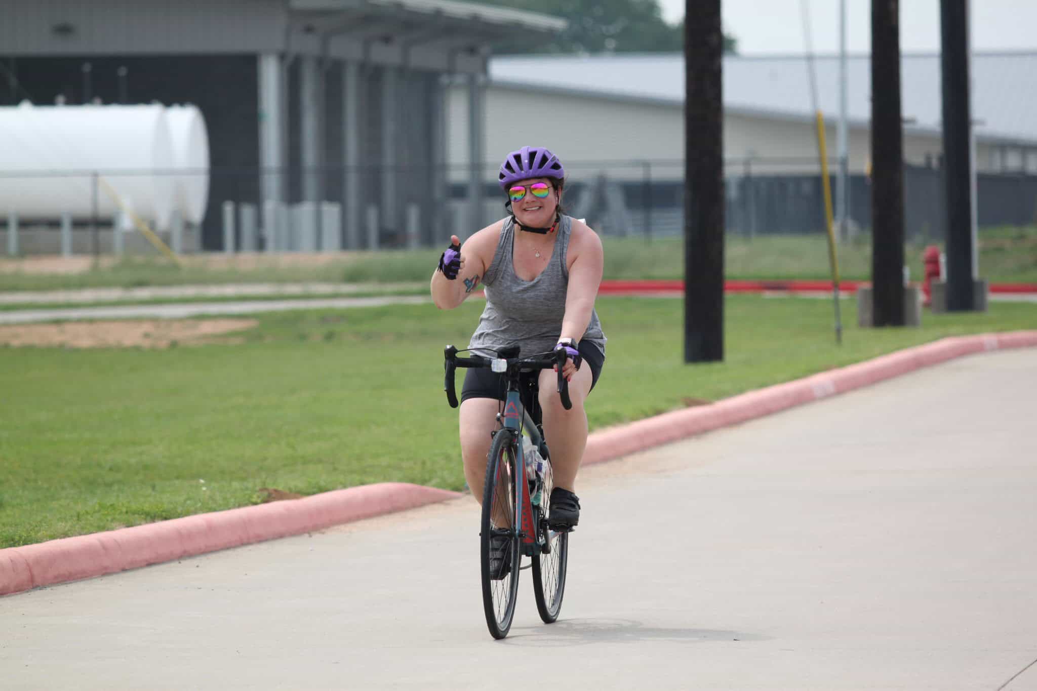Vibrant woman cycling on a trail wearing a purple helmet and sunglasses for outdoor exercise.