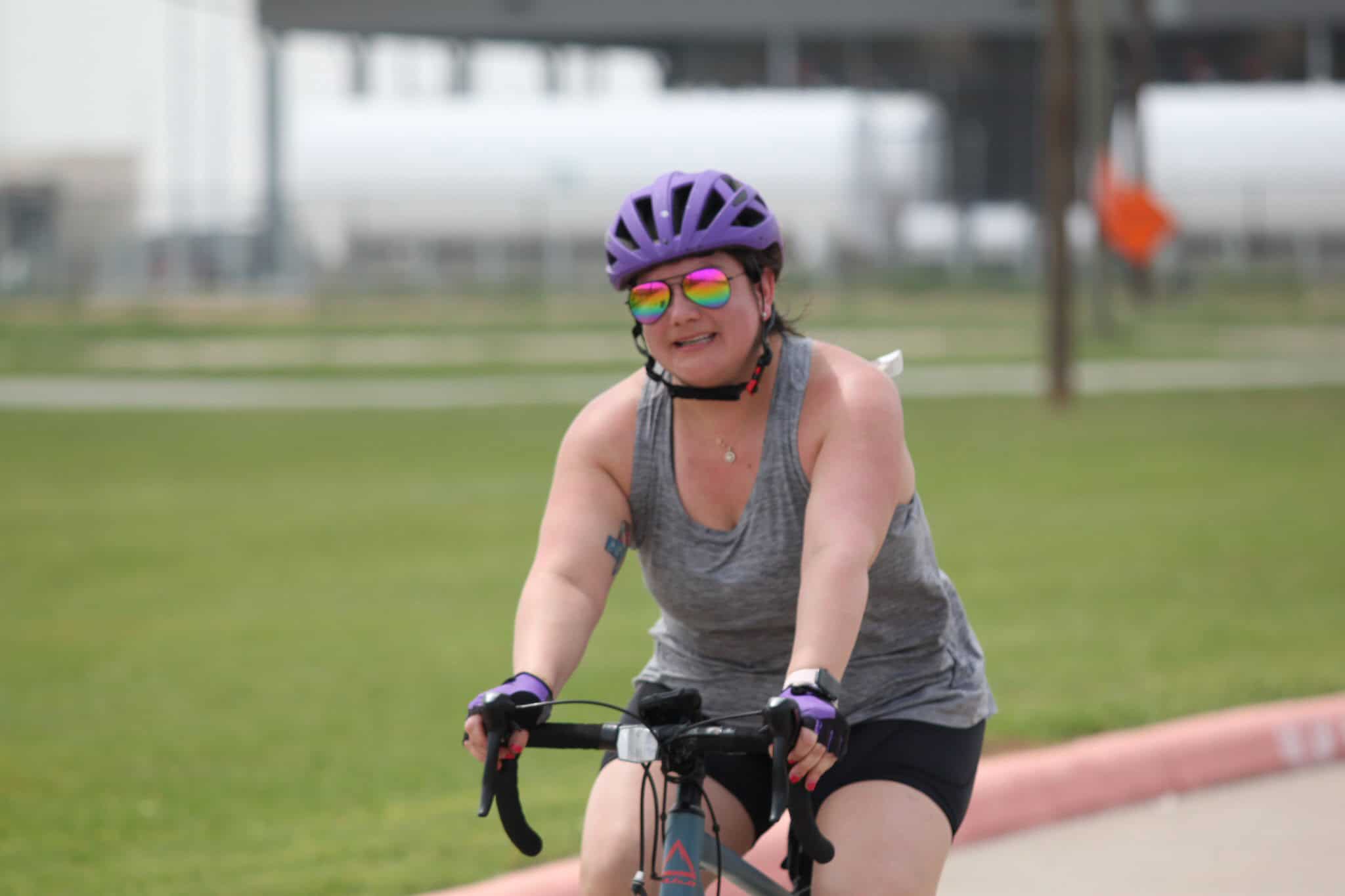 Colorful cyclist woman riding bike wearing helmet and sunglasses at Bluebonnet Express event.