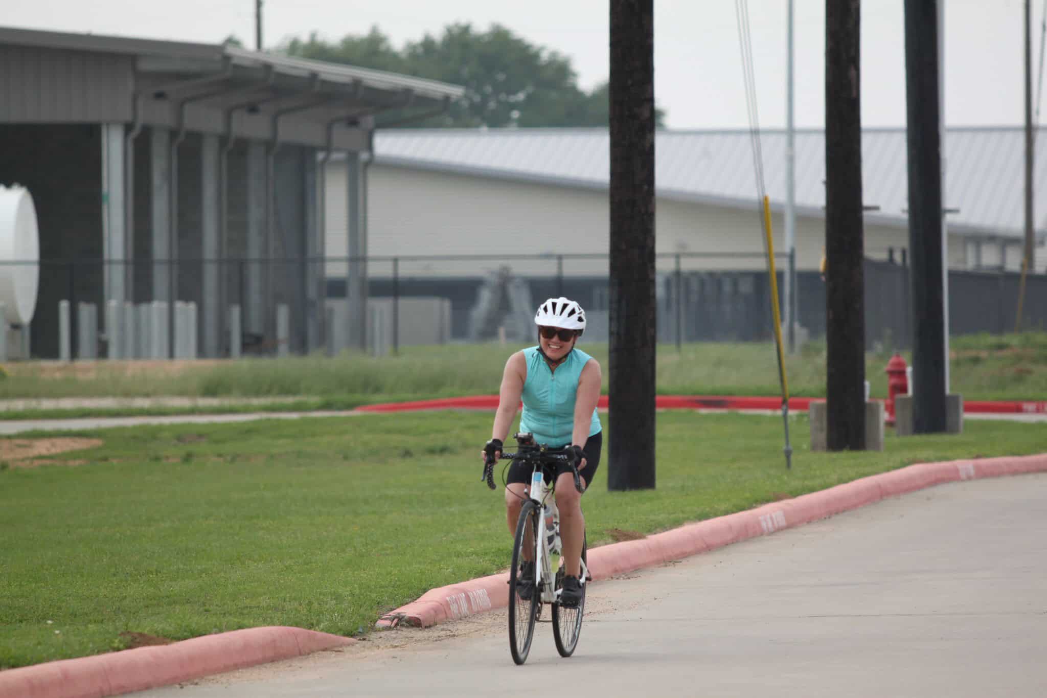 Happy woman biking on the Bluebonnet Express trail in Texas, wearing a helmet and sunglasses.
