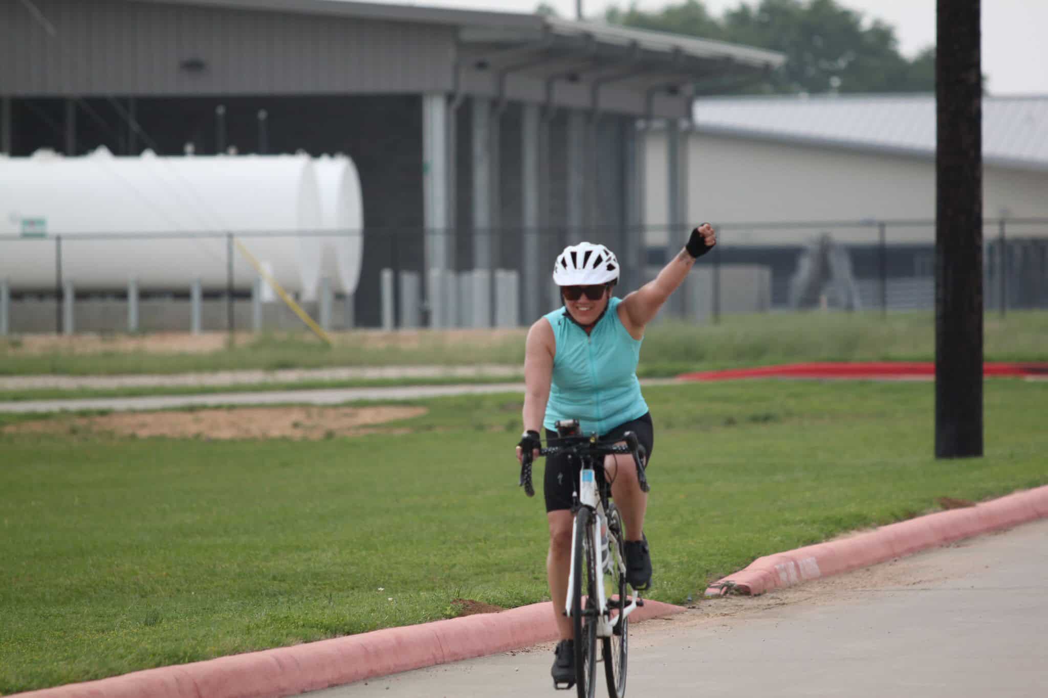Bright woman cyclist celebrating victory on a bike ride, wearing helmet and sunglasses.