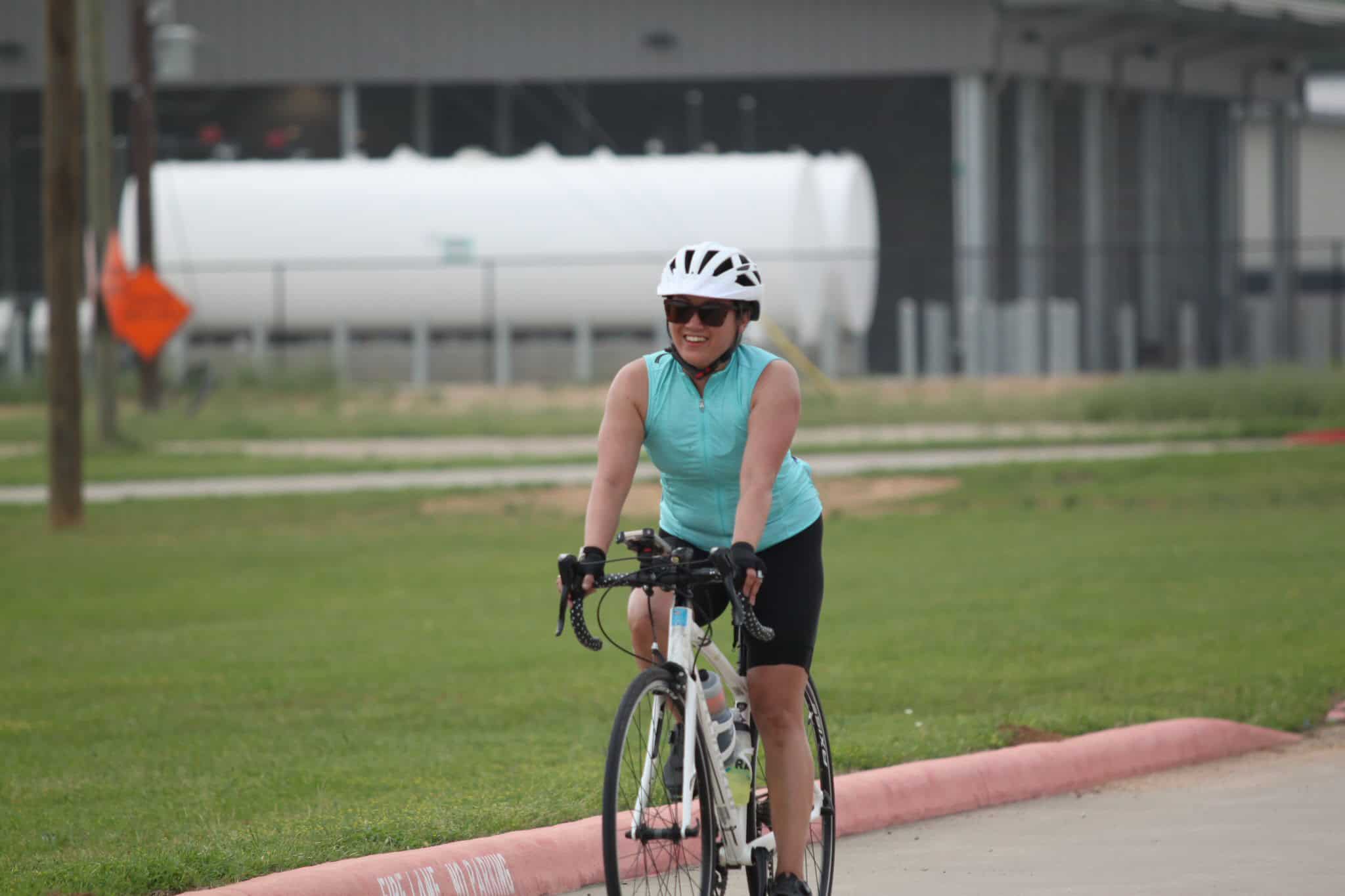 Bright smiling woman cycling on scenic bike path in protective gear, promoting Bluebonnet Express bike rides.
