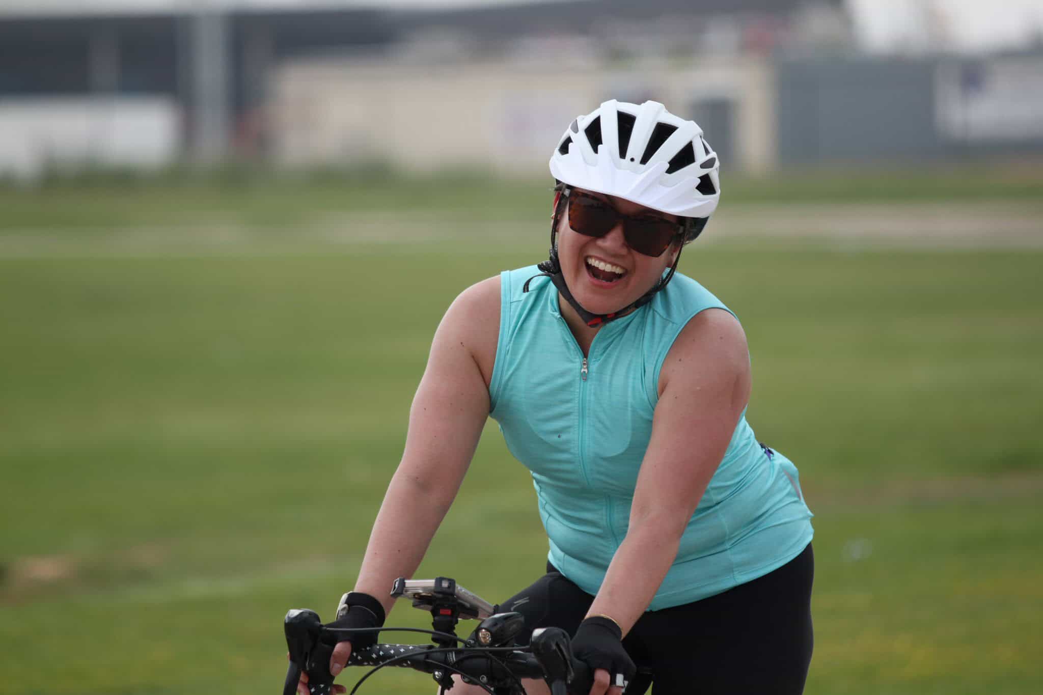 Smiling woman riding a bicycle with helmet and sunglasses, enjoying an outdoor cycling session.