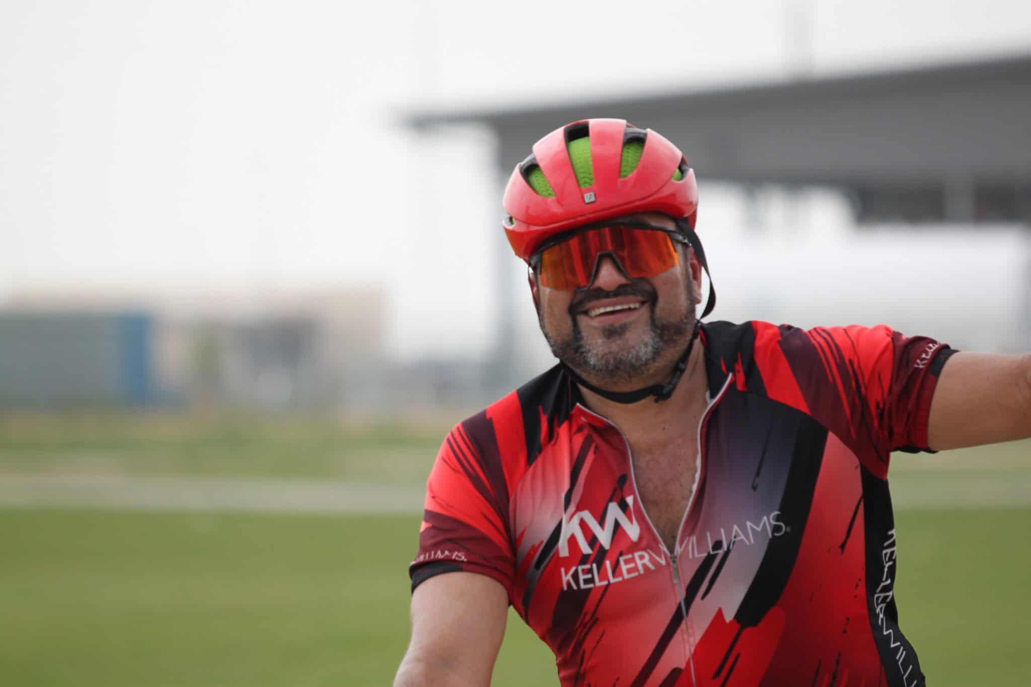 Smiling cyclist in red and black helmet and jersey, enjoying a bike ride outdoors.