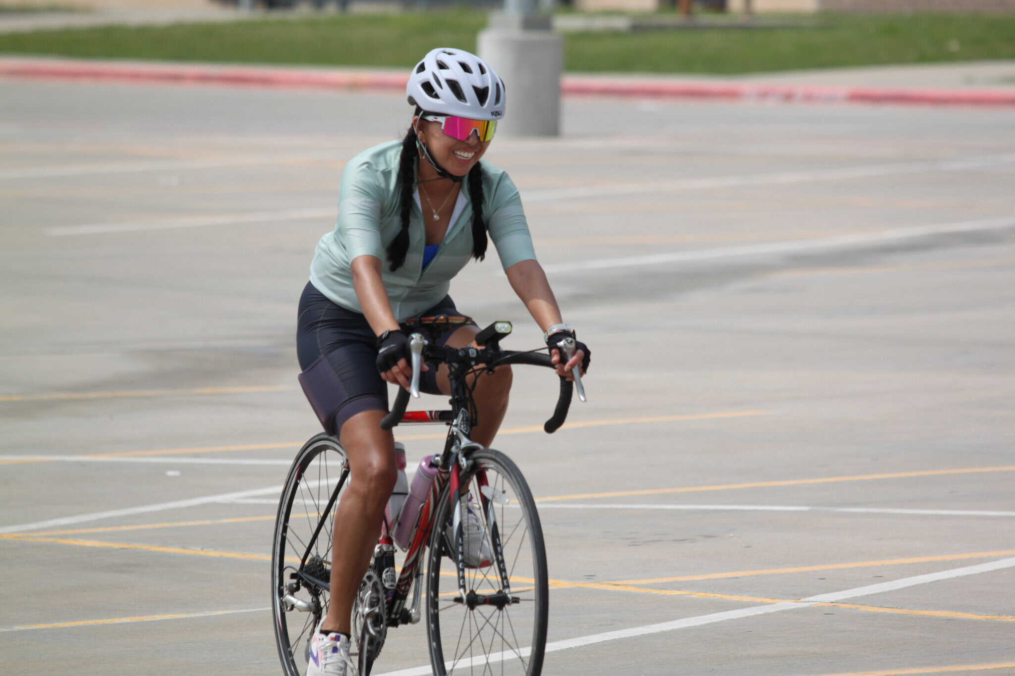 Bright woman cyclist wearing helmet and sunglasses riding a bike in open parking lot for Bluebonnet Express event.