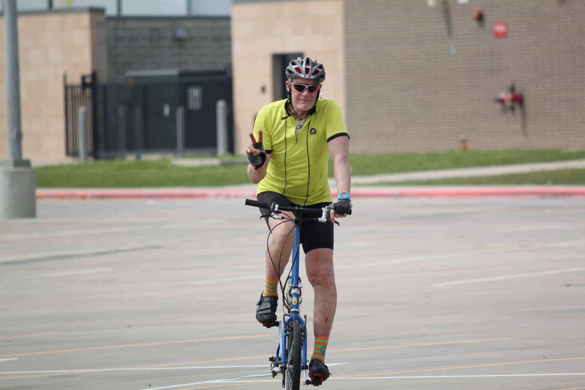 Vibrant cyclist riding Bluebonnet Express bike, making peace sign during outdoor exercise.