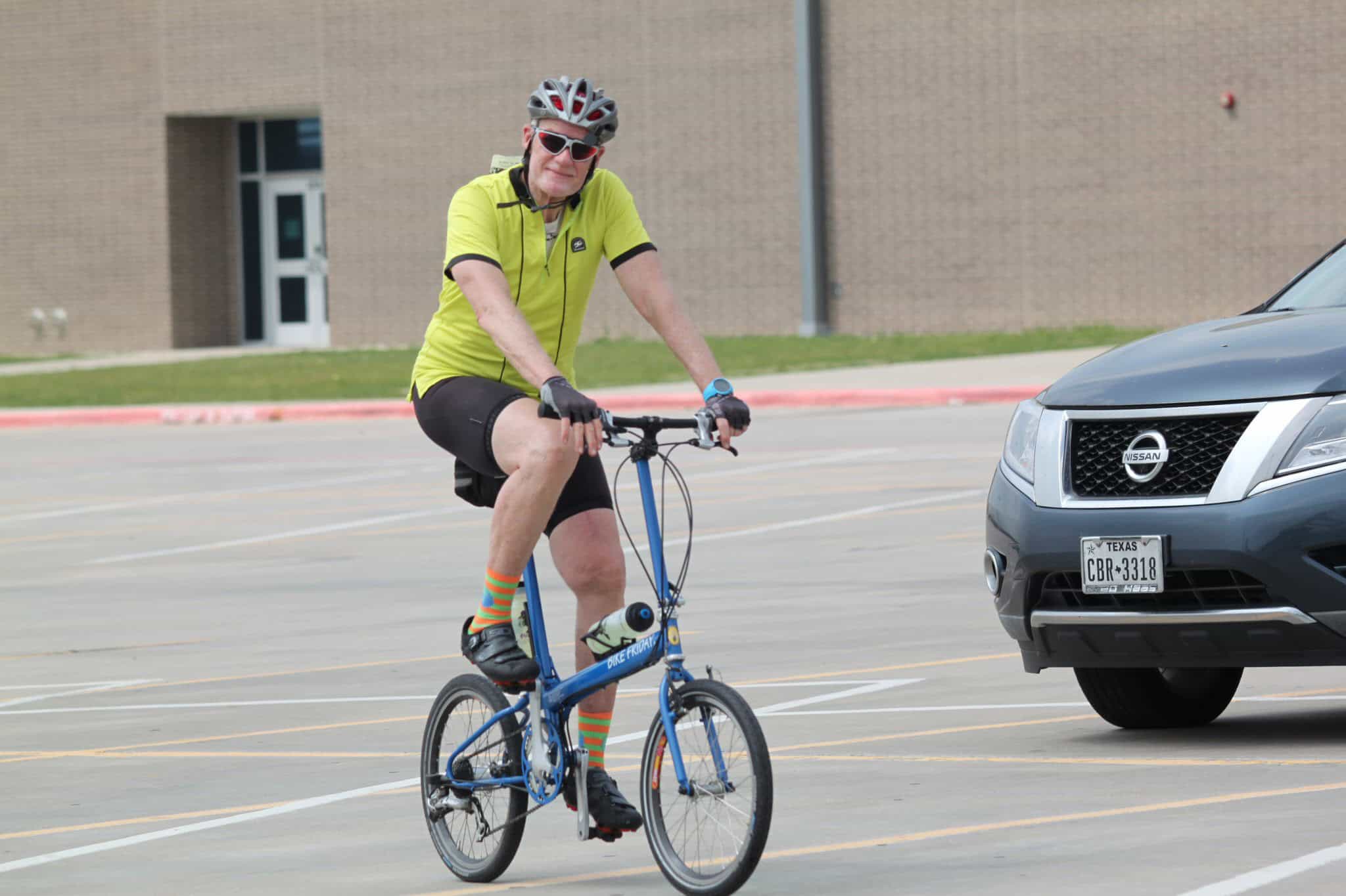 Bright yellow cycling jersey, bike rider in logoed safety gear, urban parking lot scene.