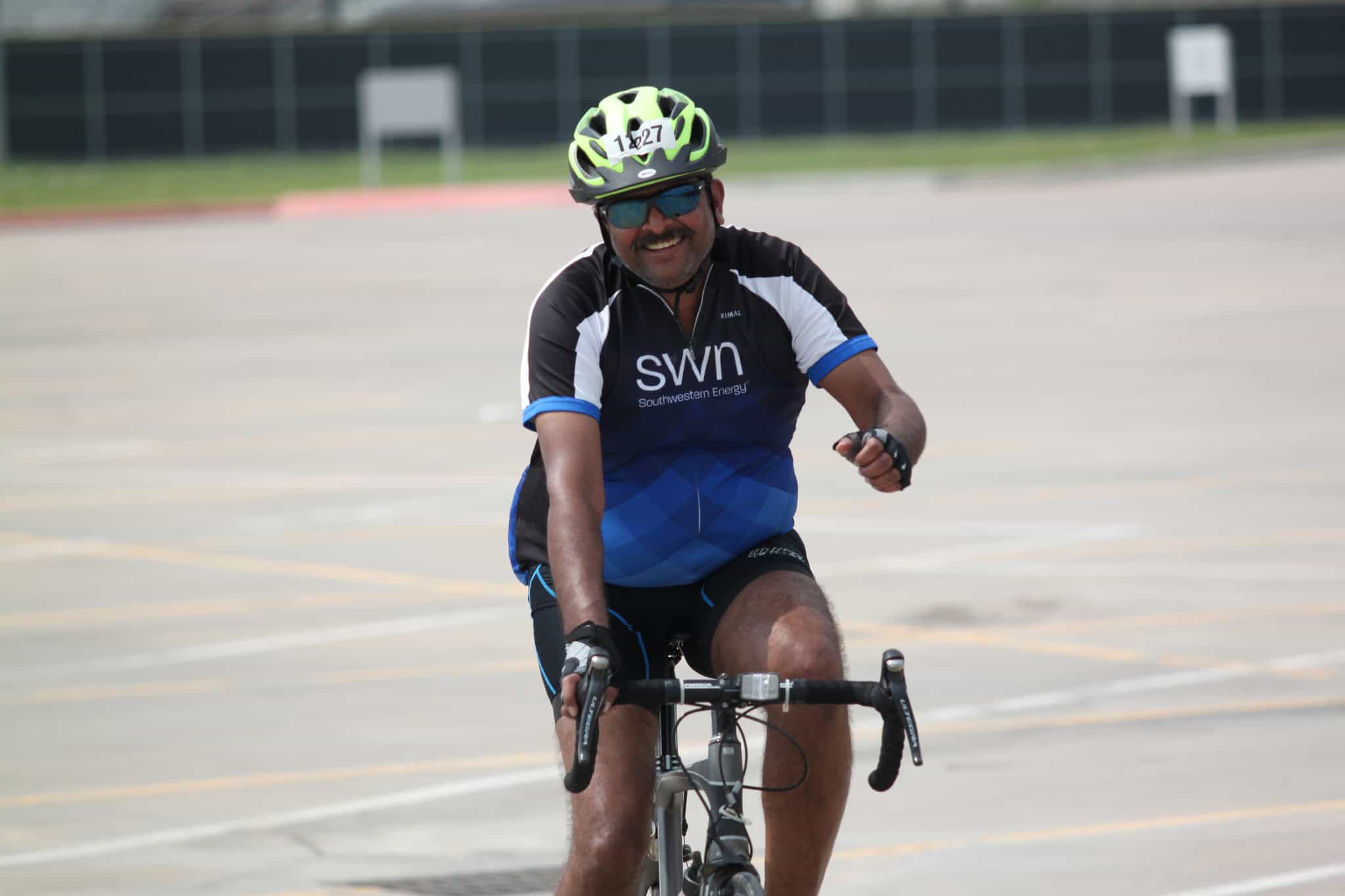Vibrant cyclist smiling during a biking event, wearing a helmet and sports attire, riding through an outdoor track.