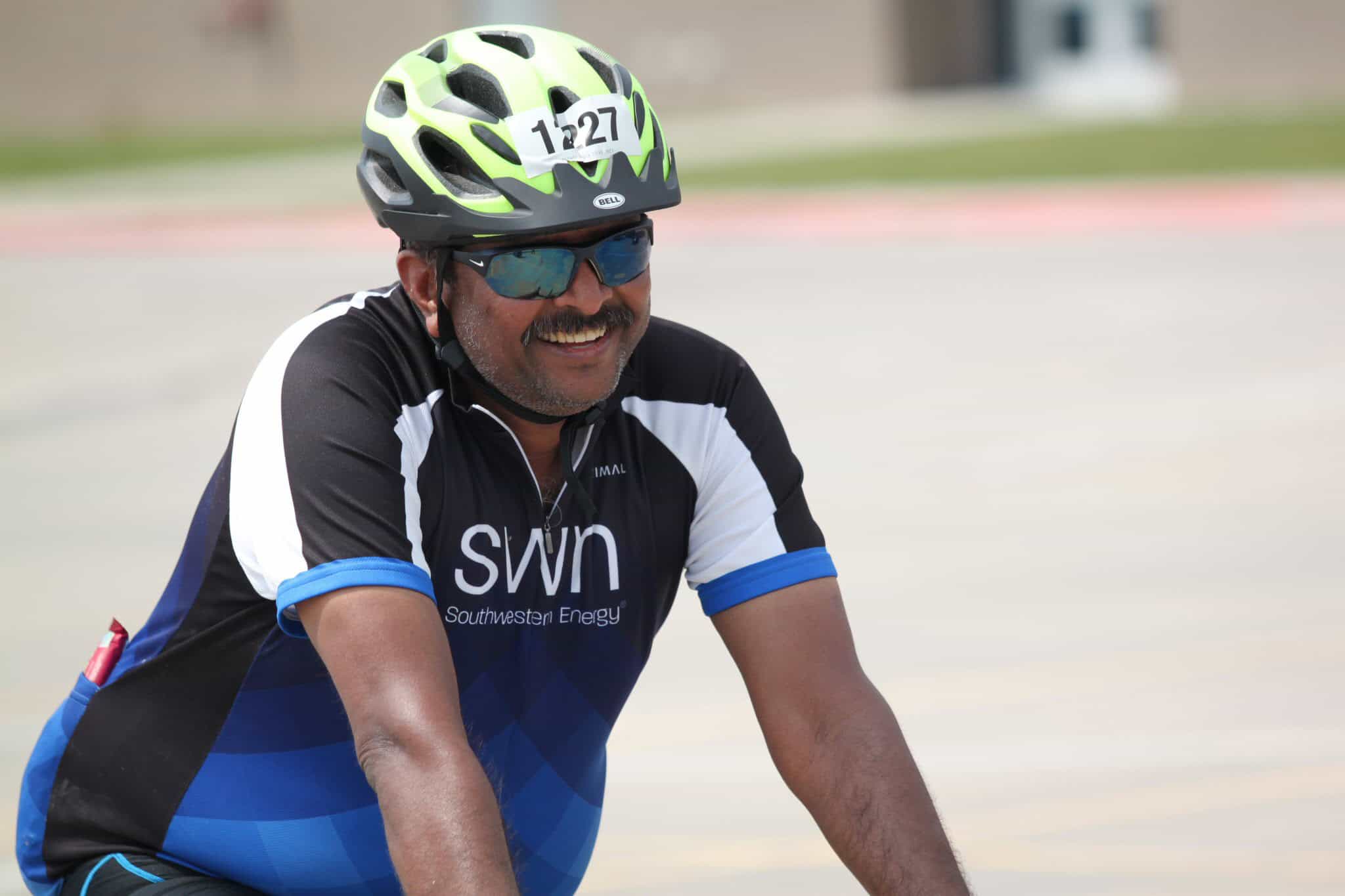 Bright smiling cyclist wearing helmet and sunglasses during outdoor bike race.