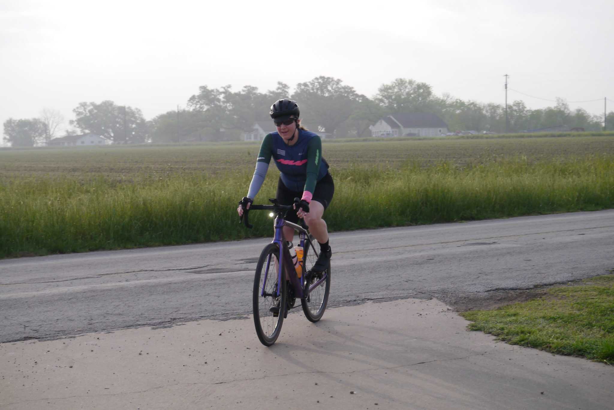Vibrant cyclist riding along rural road with green fields and trees in background, promoting Bluebonnet Express bike tours.