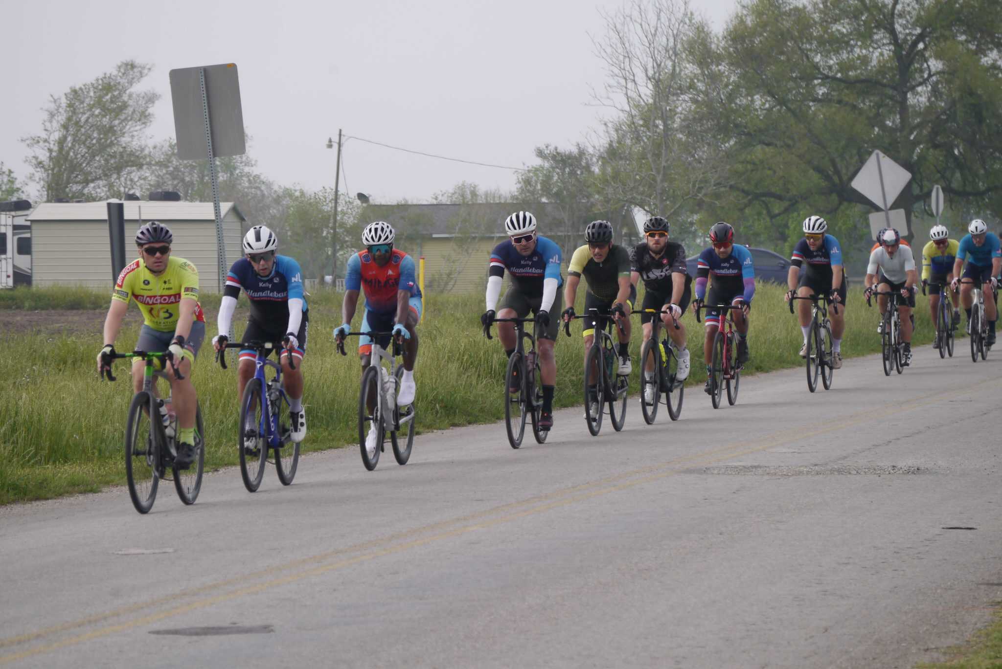 Bicycle group ride on rural road with cyclists wearing helmets and sports gear, scenic outdoor cycling adventure.