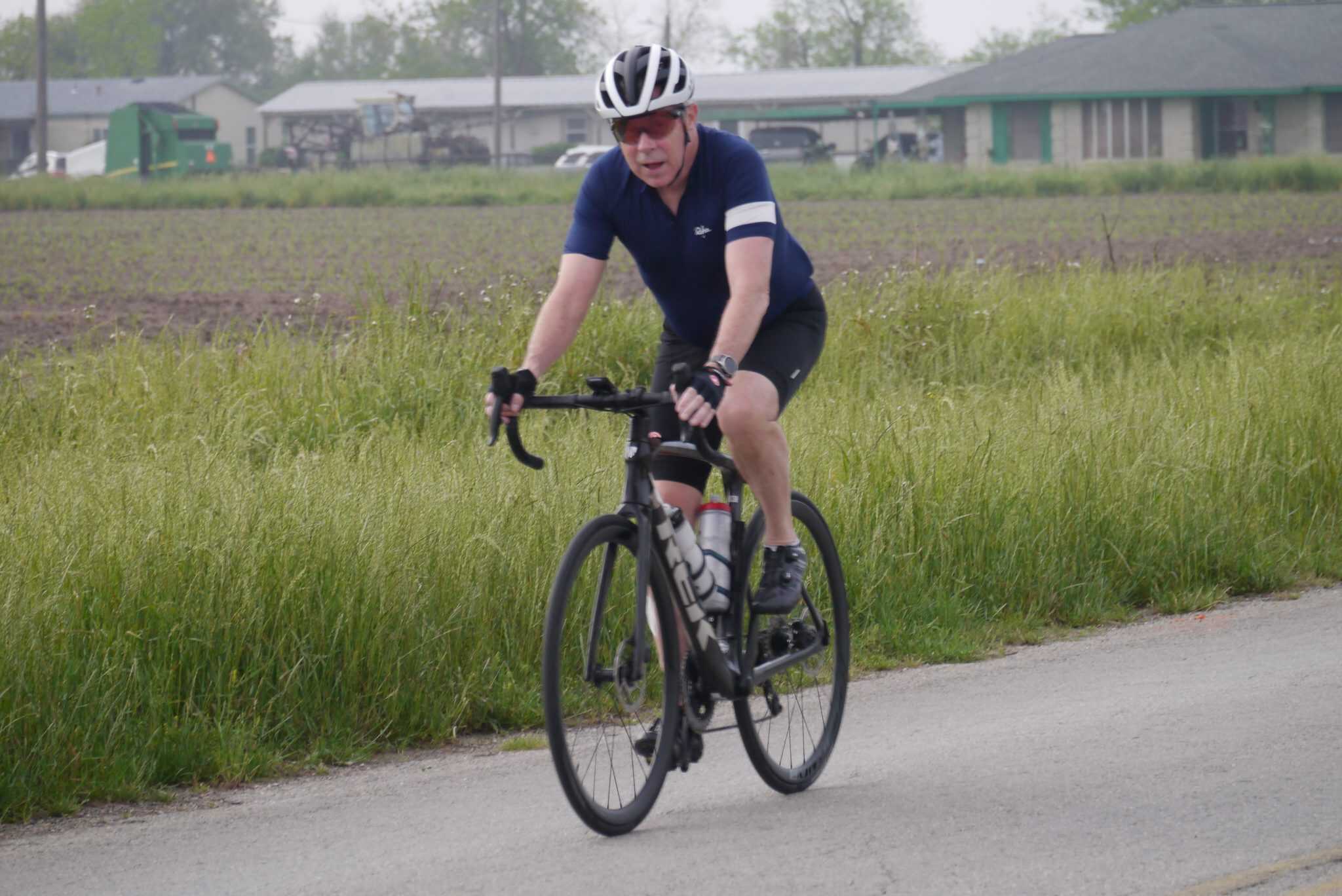 Vibrant cyclist riding a road bike on a scenic trail with green fields and suburban backdrop.