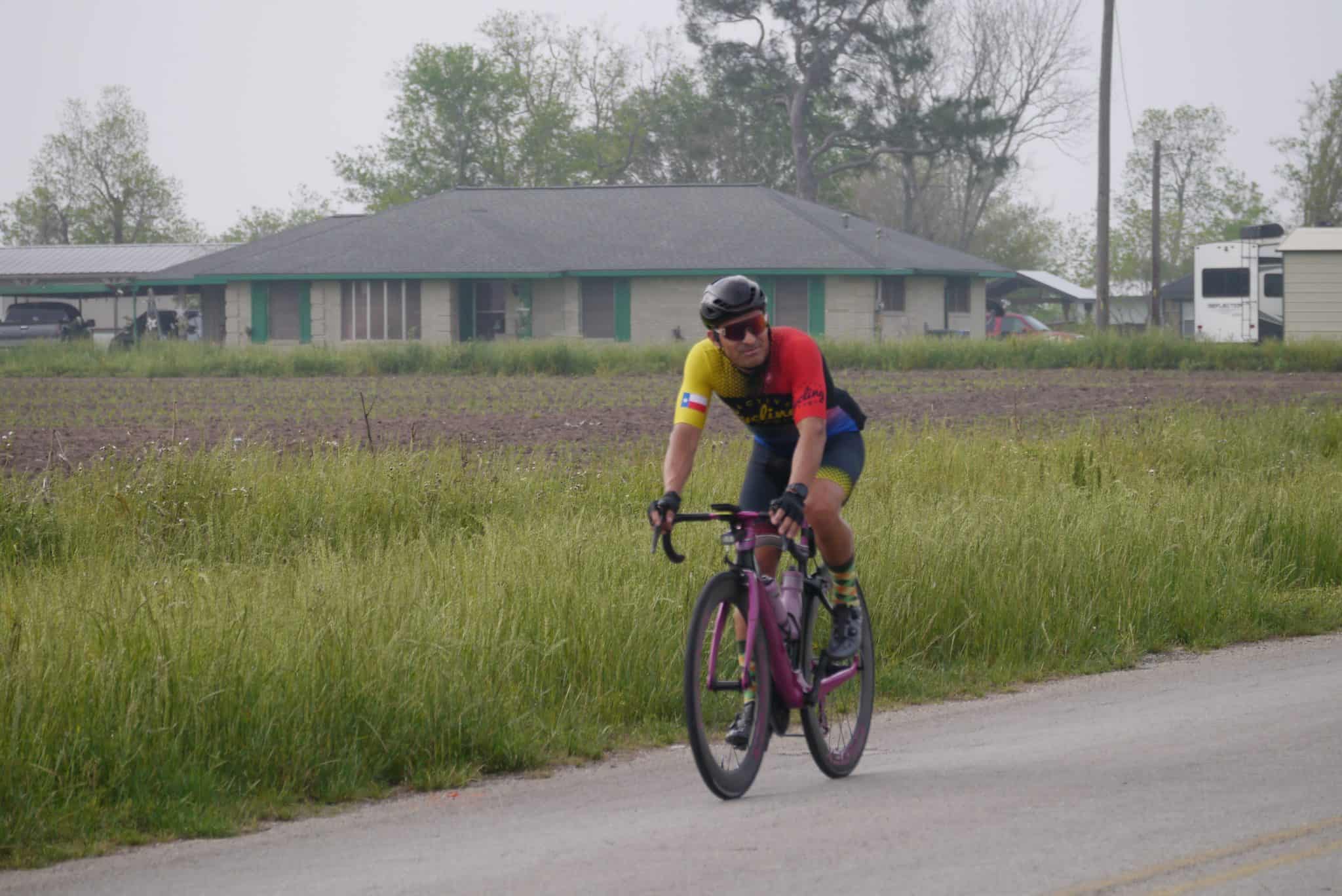Bright cyclist riding on a rural Texas road with the Bluebonnet Express sign in the background.