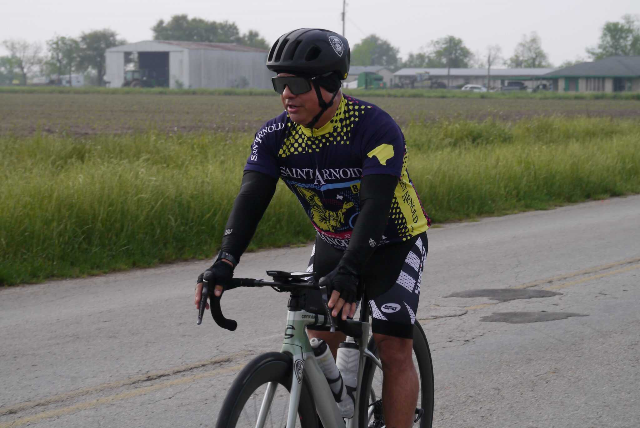 Reflective cyclist wearing Saint Arnold cycling jersey on rural road at dawn.