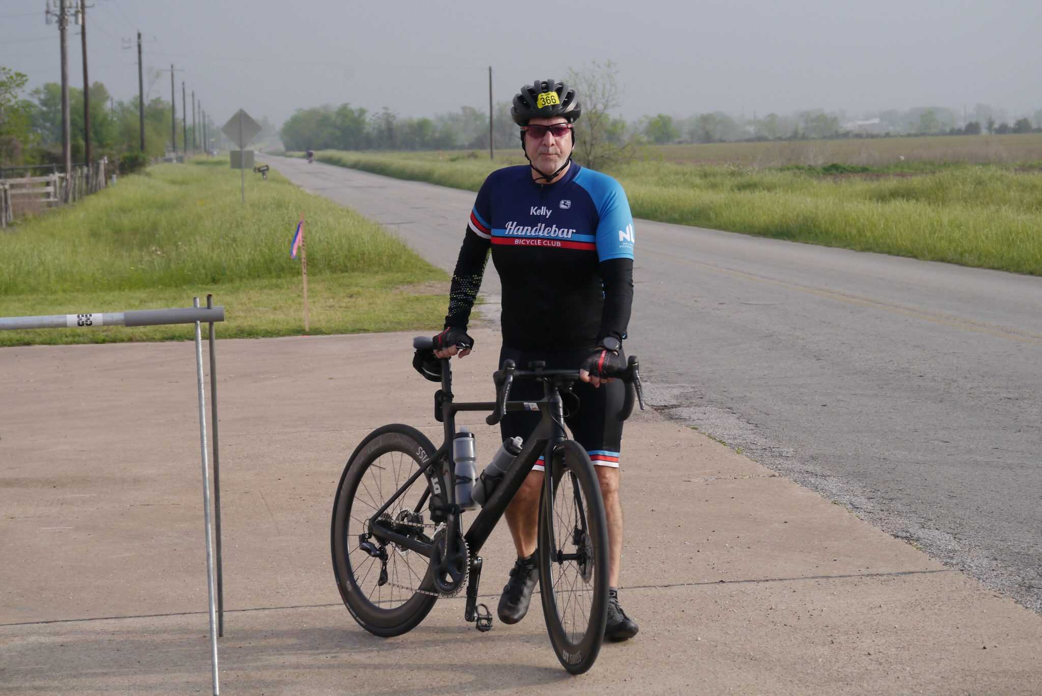 Cyclist with a black road bike on rural roadside, promoting Bluebonnet Express cycling event.
