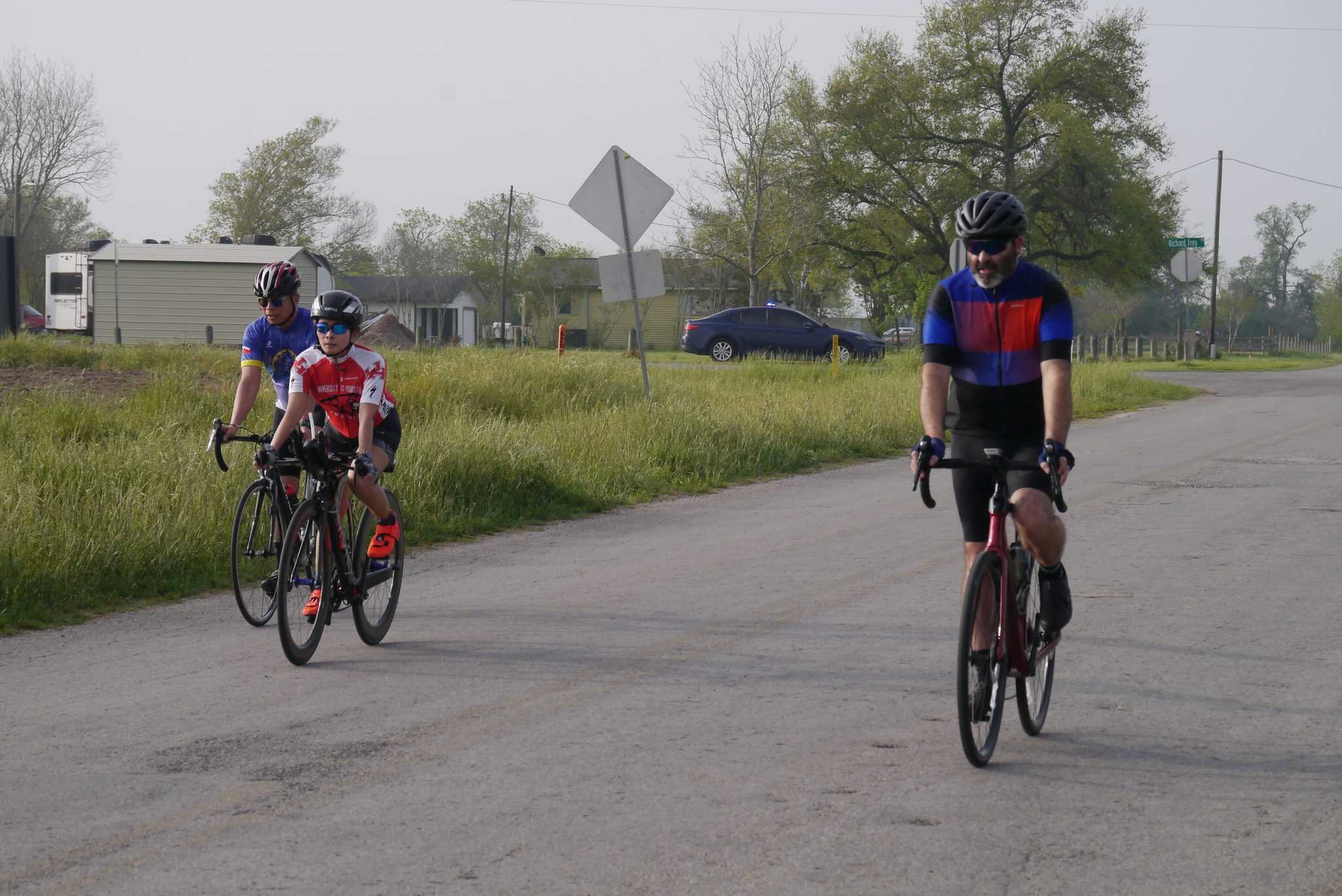 Pedestrians riding bikes along a rural road in daytime.