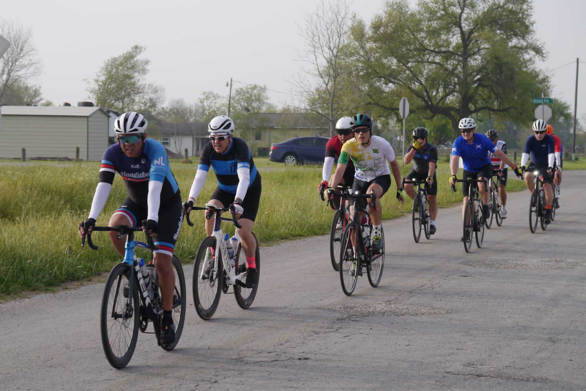 Vibrant group of cyclists riding on a scenic rural route with Greenery, promoting Bluebonnet Express bike tours.