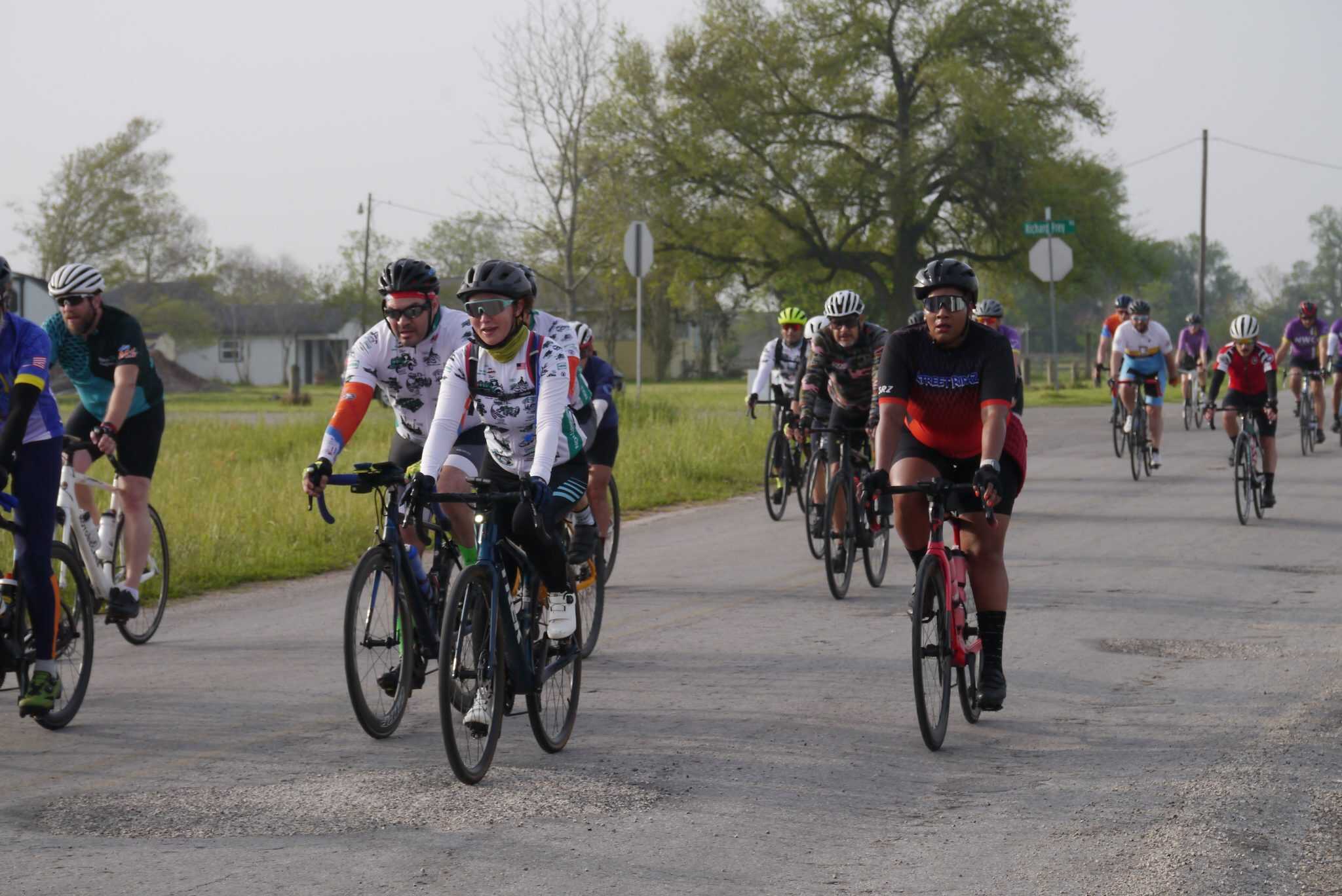 Group of cyclists riding on open road during daytime, promoting Bluebonnet Express cycling event.