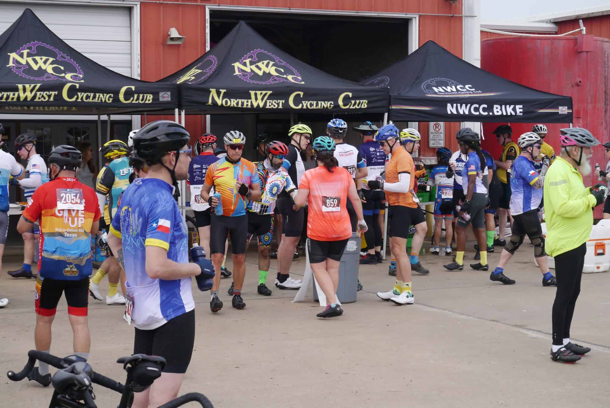 Cycling event at NWCC with riders preparing, wearing colorful jerseys, and gathering under NorthWest Cycling Club tents.