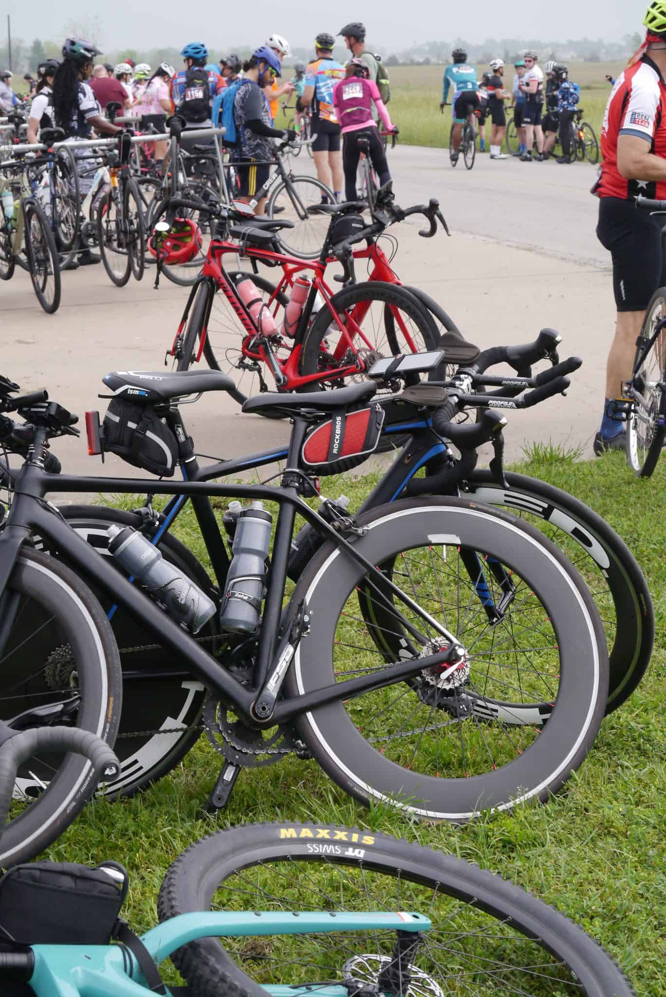 Bike rack with colorful bikes at Bluebonnet Express cycling event, surrounded by cyclists and outdoor scenery.