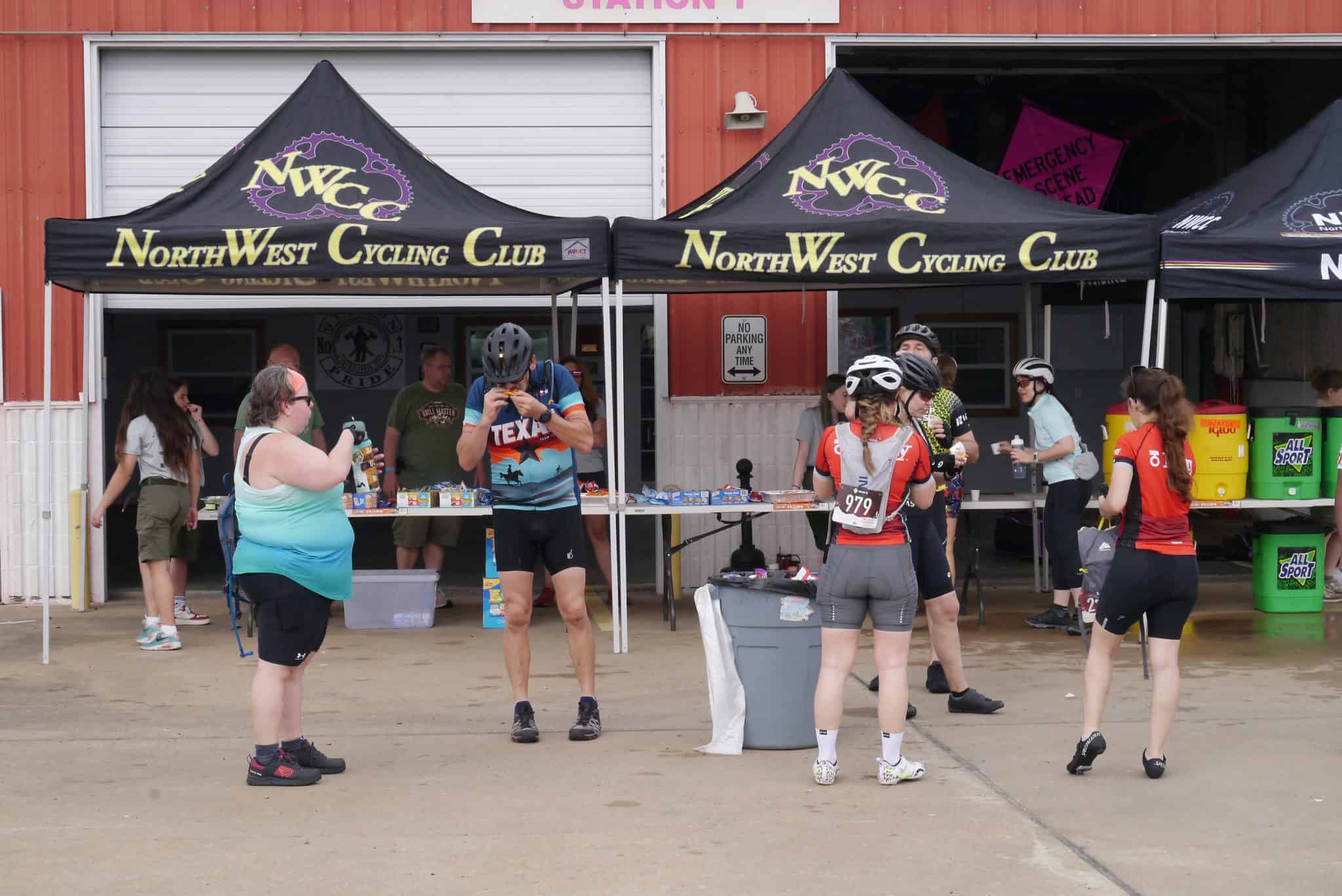 Cyclists at NorthWest Cycling Club event, aid station with volunteers, hydration, snacks, and race support.