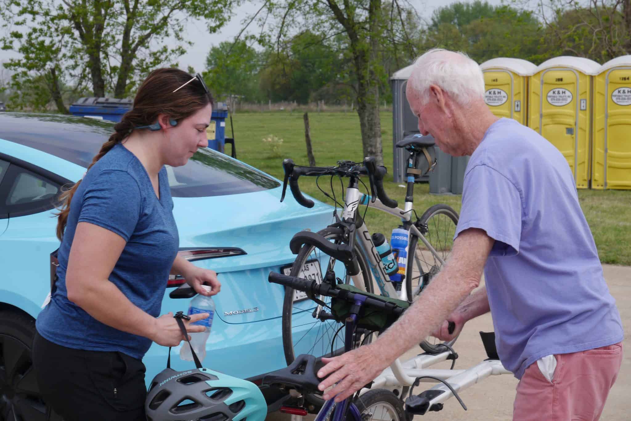 Young woman and elderly man preparing bikes for Bluebonnet Express bike ride, outdoor scene.