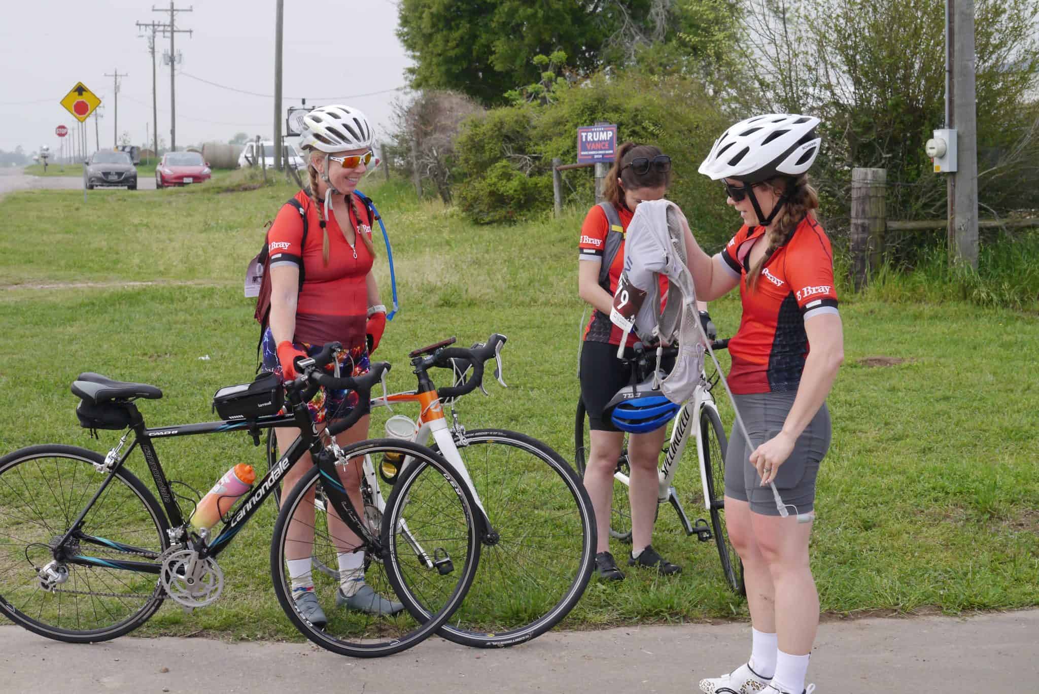 Female cyclists in team jerseys prepare for a ride on a bike trail.