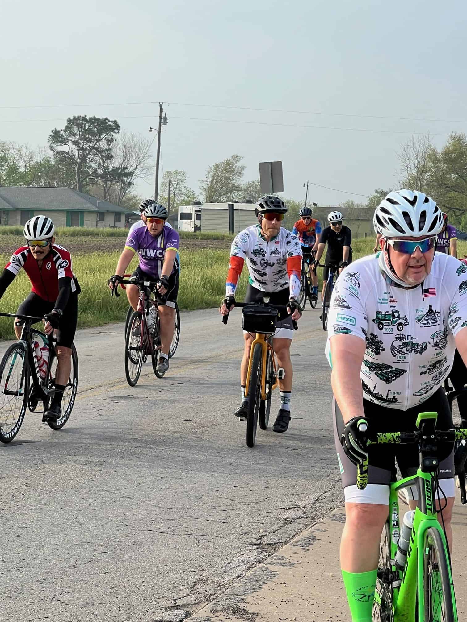 Colorful group cycling event during daytime with enthusiastic bikers on a rural road, showcasing Bluebonnet Express biking experience.