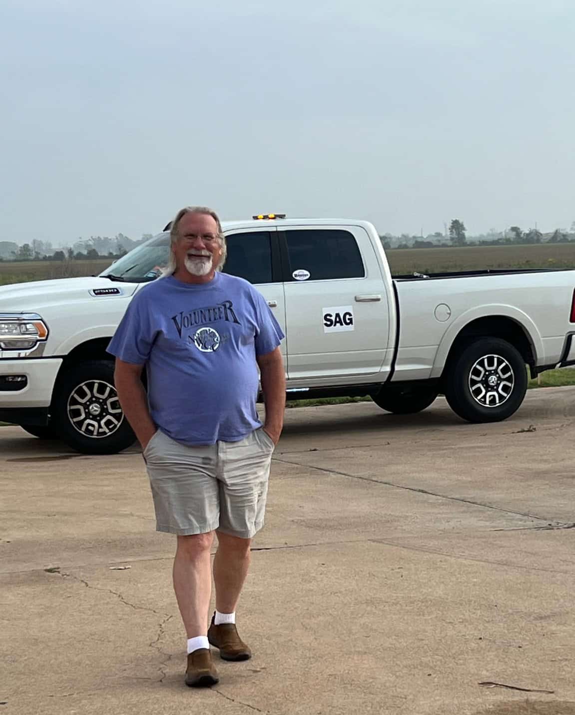 Man standing outdoors with a white SAG volunteer truck in the background, on a concrete surface.