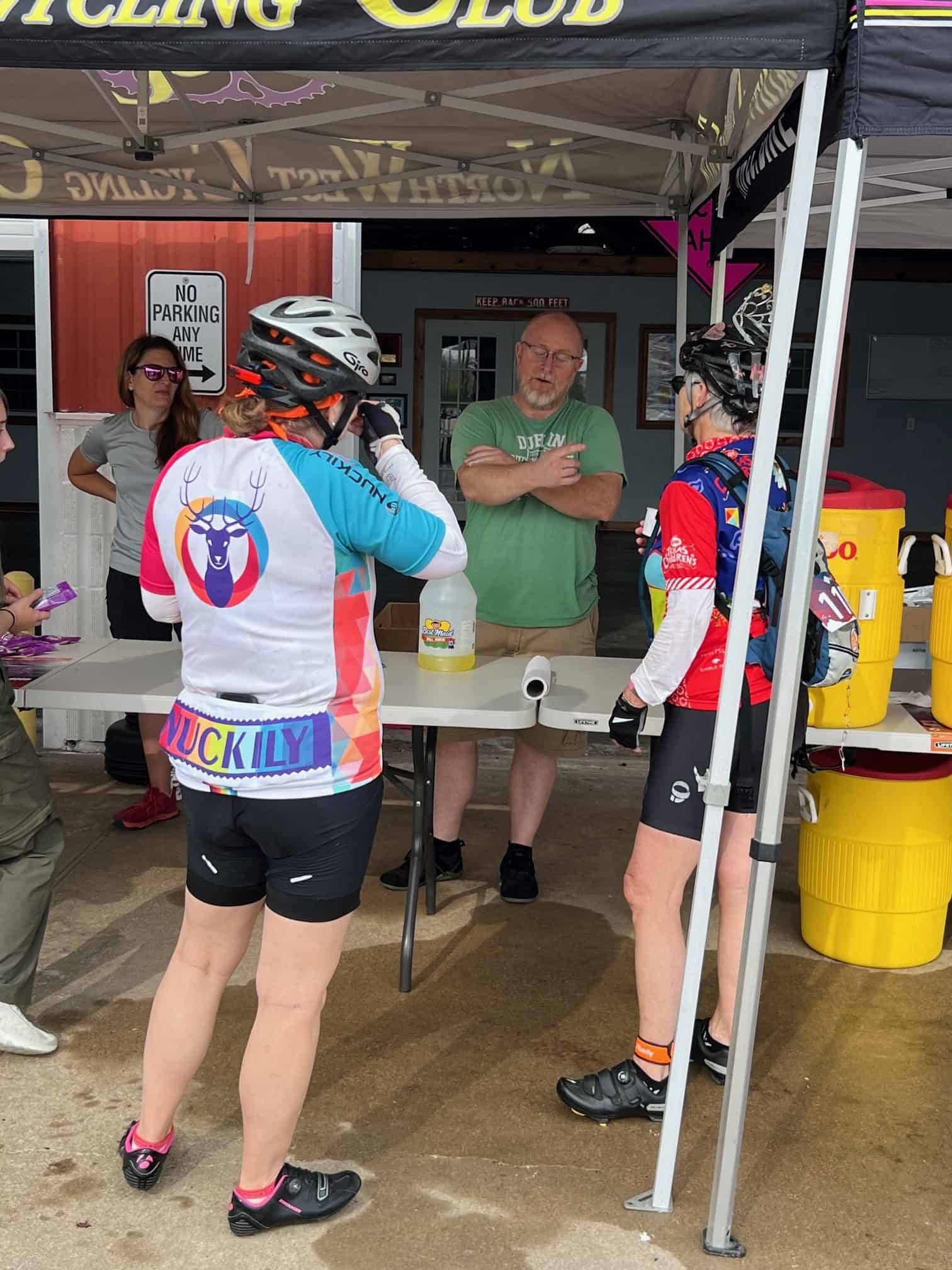 Cycling event at Bluebonnet Express with cyclists in gear, engaging with staff under a canopy.