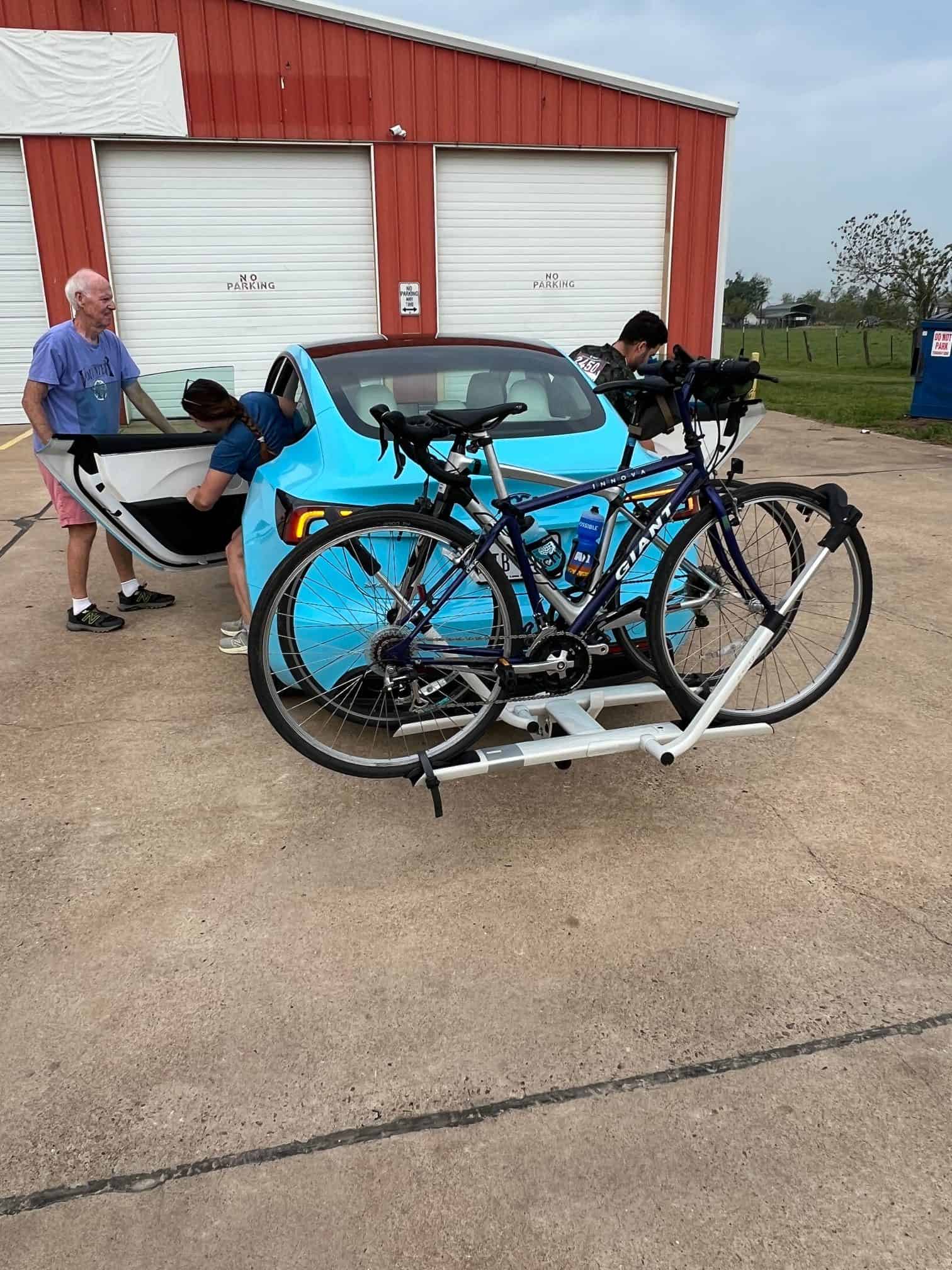 Bicycle rack attachment for car with blue car and people loading bikes.