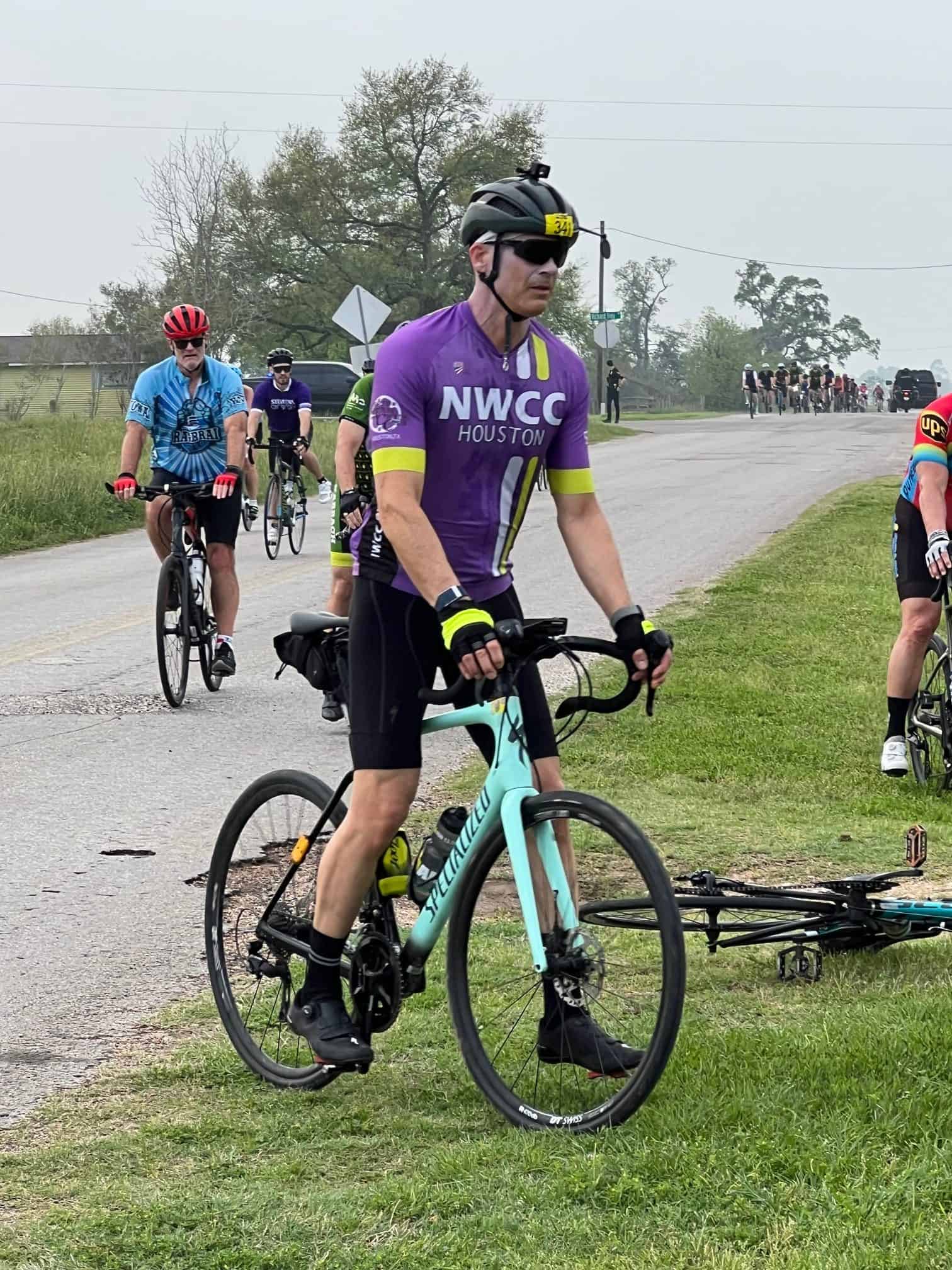 Bicycle group riding event on a scenic rural road during daytime, featuring cyclists in colorful jerseys and gear.