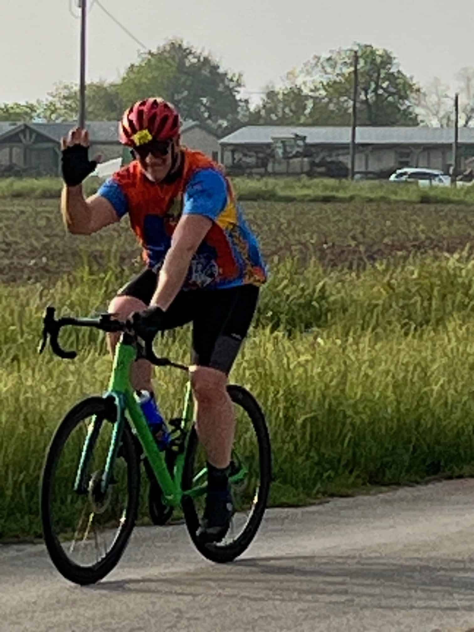 Vibrant cyclist riding a green bike with a helmet and colorful attire on a scenic road.