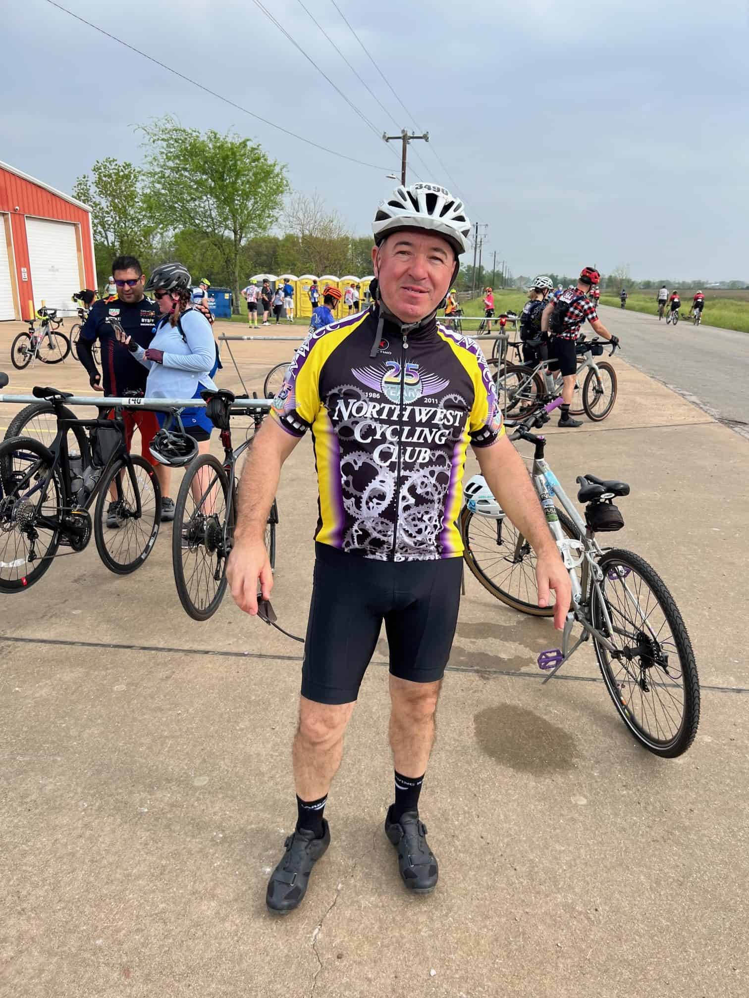 Adult male cyclist in colorful jersey standing with bike at Bluebonnet Express event.