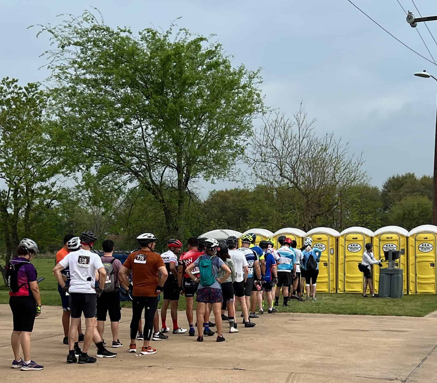 Waiting in line for the Bluebonnet Express bike event, cyclists gather outdoors in a scenic park setting.